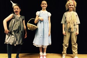 Child actors on stage as the Tin Man, Dorothy and the Scarecrow