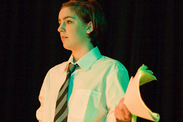 A teenage girl on stage holding a script